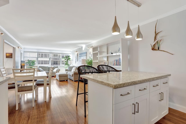 kitchen with a breakfast bar, hanging light fixtures, open floor plan, white cabinetry, and wood finished floors