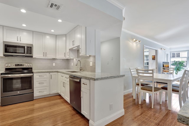 kitchen featuring light wood finished floors, stainless steel appliances, decorative backsplash, white cabinetry, and a sink