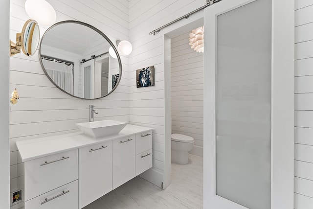 bathroom with vanity, wood walls, and toilet