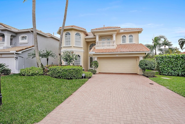 mediterranean / spanish home featuring a balcony, a tile roof, decorative driveway, stucco siding, and a front yard