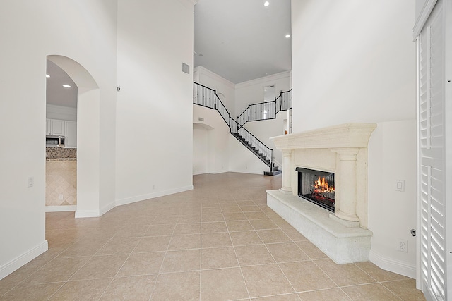 unfurnished living room featuring a high end fireplace, a towering ceiling, baseboards, and light tile patterned floors