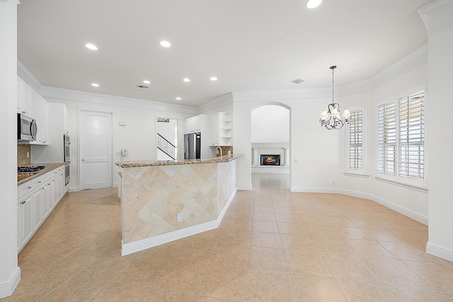 kitchen with stone countertops, ornamental molding, a lit fireplace, stainless steel appliances, and white cabinetry