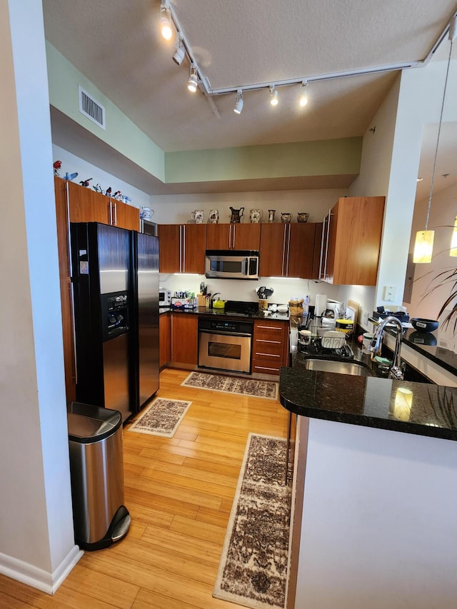 1551 N Flagler Dr Ph L7, West Palm Beach, FL 33401 - kitchen with stainless steel appliances, rail lighting, a sink, light wood-style flooring, and dark stone counters