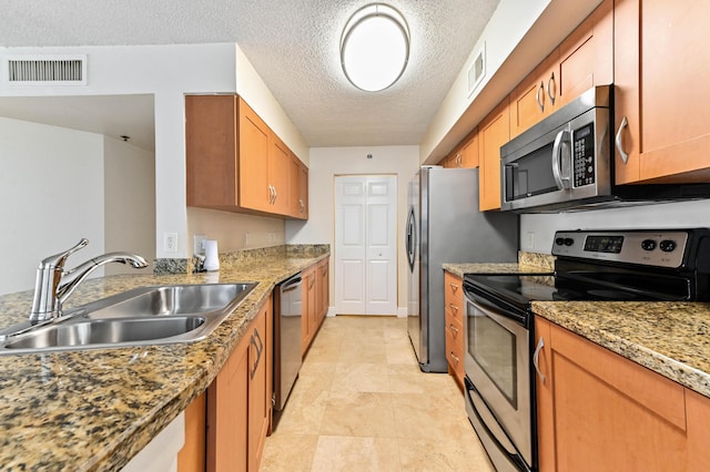 kitchen featuring light stone counters, stainless steel appliances, sink, and a textured ceiling