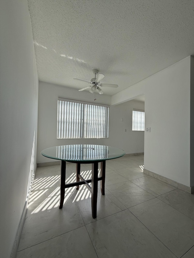 unfurnished dining area with ceiling fan and a textured ceiling