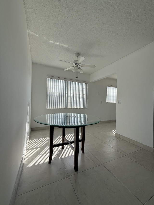 unfurnished dining area featuring ceiling fan and a textured ceiling