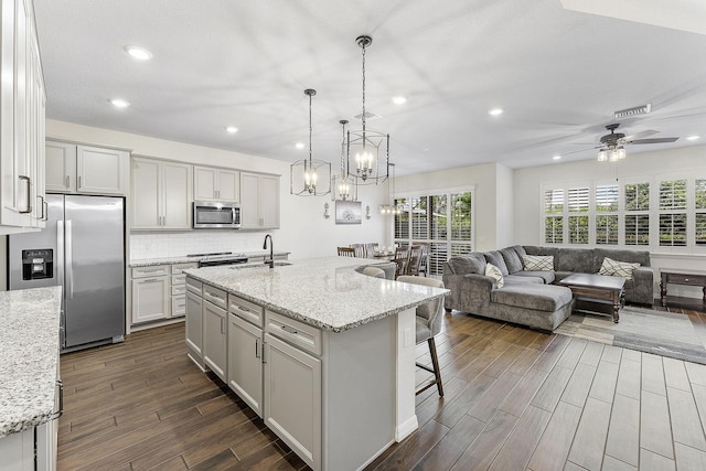 kitchen with an island with sink, light stone countertops, appliances with stainless steel finishes, and open floor plan