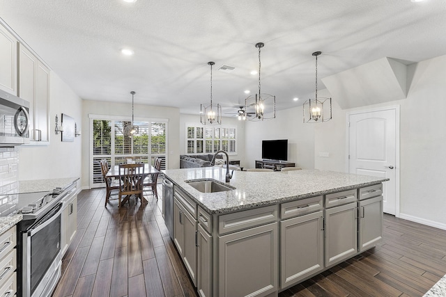 kitchen with a center island with sink, stainless steel appliances, gray cabinets, hanging light fixtures, and a sink