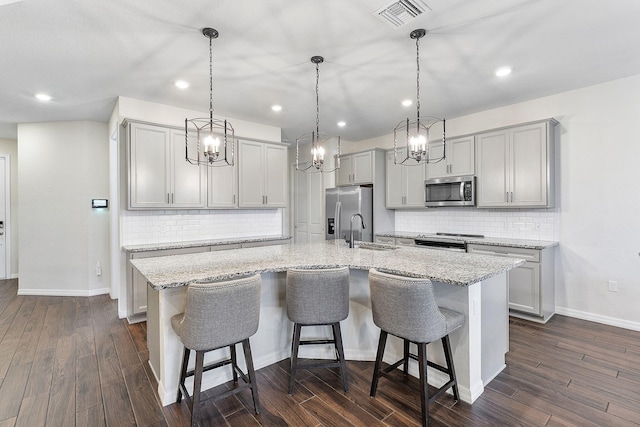 kitchen with visible vents, hanging light fixtures, a kitchen island with sink, gray cabinets, and stainless steel appliances