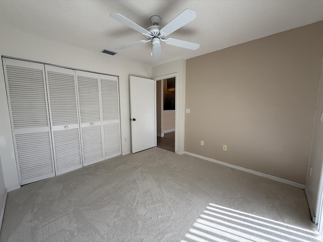 unfurnished bedroom with ceiling fan, light carpet, a textured ceiling, and a closet