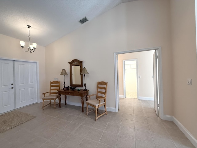 foyer featuring an inviting chandelier, light tile patterned floors, high vaulted ceiling, and a textured ceiling