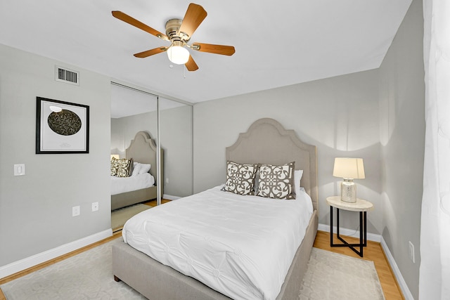 bedroom with a closet, wood finished floors, visible vents, and baseboards