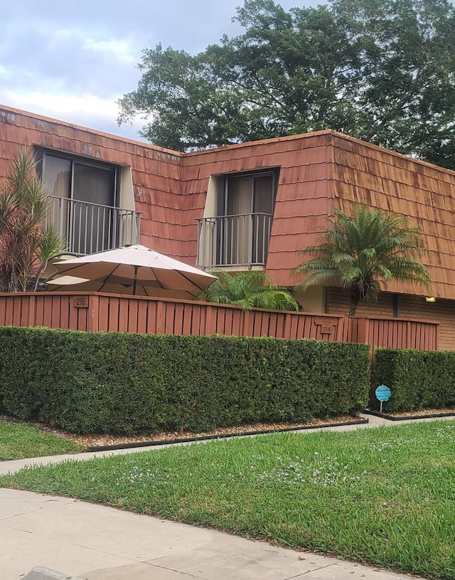 view of side of property featuring brick siding, a yard, and mansard roof