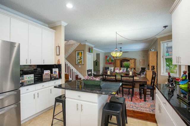 kitchen with white cabinetry, crown molding, a kitchen breakfast bar, and stainless steel refrigerator