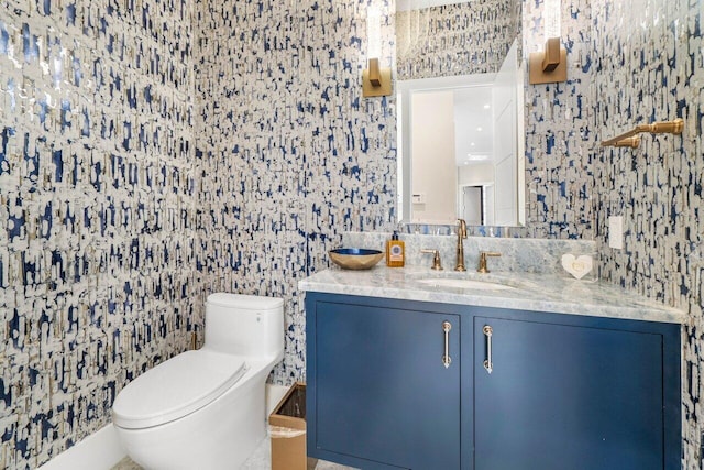 half bath with vanity, toilet, and wallpapered walls