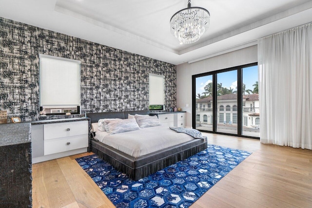 bedroom featuring access to outside, a tray ceiling, light wood-style floors, and wallpapered walls