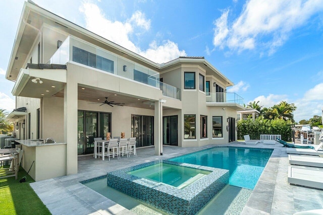 back of property featuring outdoor dry bar, stucco siding, a pool with connected hot tub, ceiling fan, and a balcony