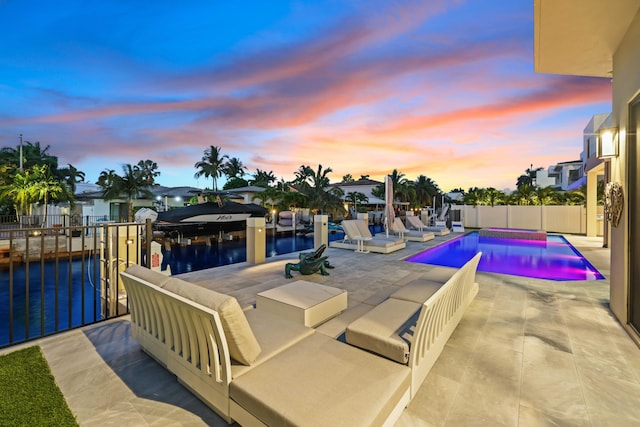 pool at dusk with a patio, a water view, fence, and a fenced in pool