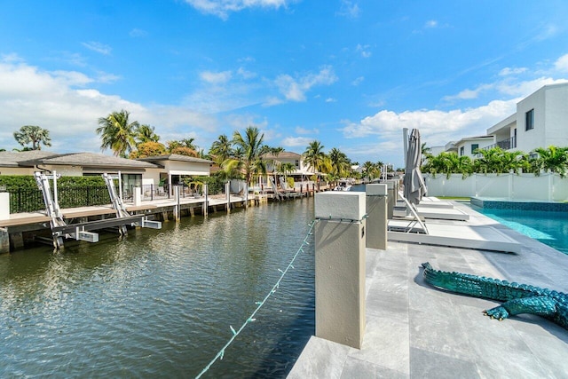 dock area featuring boat lift, a water view, fence, and a fenced in pool