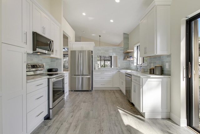 kitchen featuring vaulted ceiling, stainless steel appliances, light countertops, open shelves, and a sink