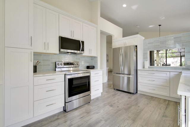 kitchen with stainless steel appliances, white cabinets, vaulted ceiling, light wood finished floors, and tasteful backsplash