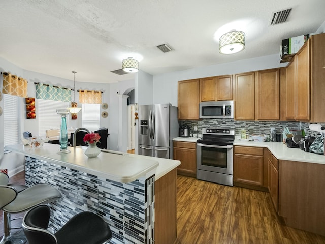 kitchen with pendant lighting, stainless steel appliances, dark hardwood / wood-style floors, tasteful backsplash, and kitchen peninsula