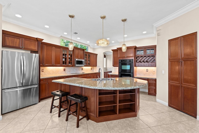 kitchen featuring a center island with sink, light stone counters, black appliances, decorative light fixtures, and sink