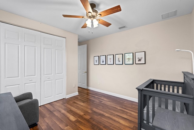 bedroom with dark wood-type flooring, a nursery area, ceiling fan, and a closet