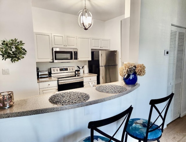 kitchen with appliances with stainless steel finishes, pendant lighting, white cabinetry, a kitchen breakfast bar, and light hardwood / wood-style floors