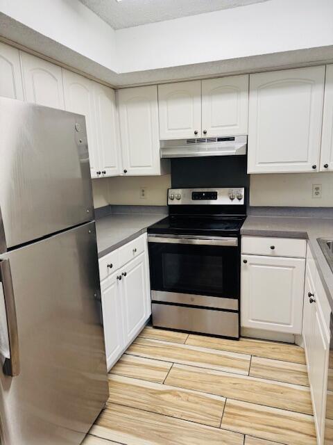 kitchen with appliances with stainless steel finishes, white cabinets, and under cabinet range hood