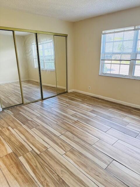 unfurnished bedroom with light wood-type flooring, a closet, multiple windows, and a textured ceiling