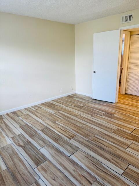 empty room featuring light wood-style floors, baseboards, visible vents, and a textured ceiling