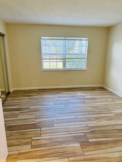 spare room featuring a textured ceiling, wood finished floors, and baseboards