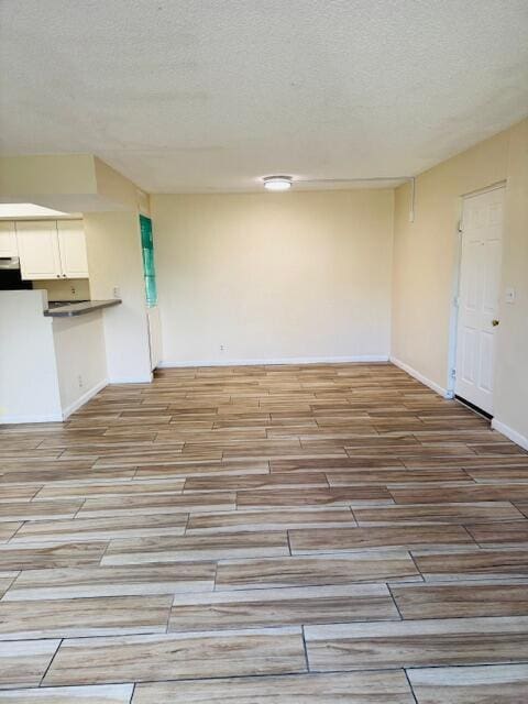 unfurnished living room featuring baseboards, a textured ceiling, and light wood finished floors