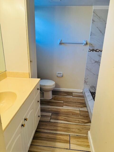 full bath with toilet, wood finished floors, vanity, baseboards, and tiled shower