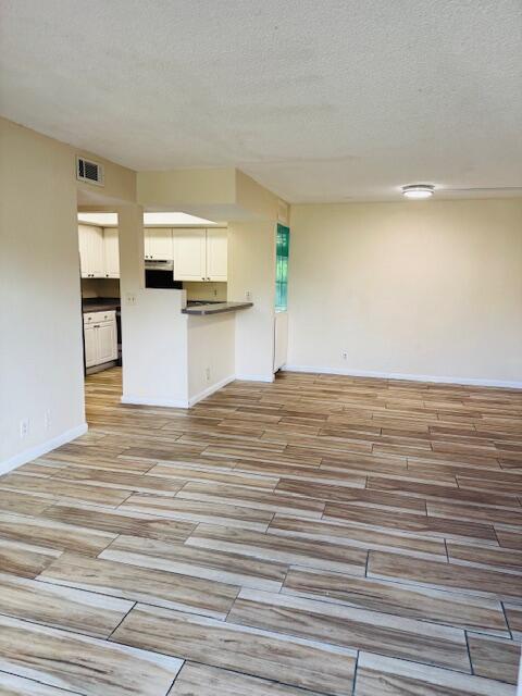 kitchen featuring visible vents, open floor plan, a textured ceiling, and wood finish floors