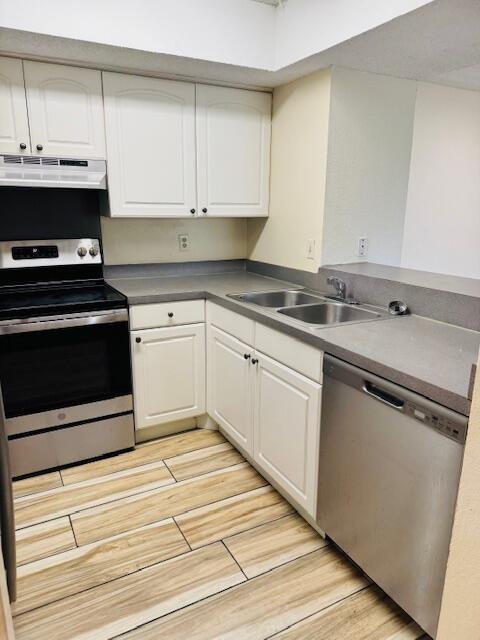 kitchen with light wood-style flooring, stainless steel appliances, a sink, white cabinetry, and range hood