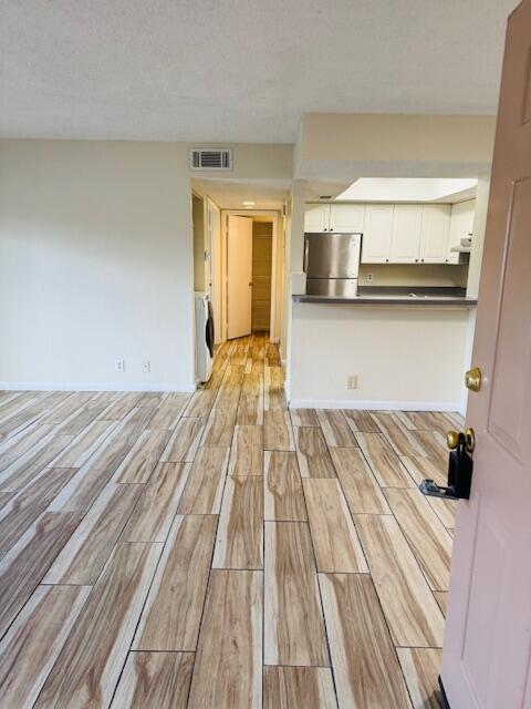 unfurnished living room with a textured ceiling, wood finish floors, visible vents, baseboards, and washer / clothes dryer