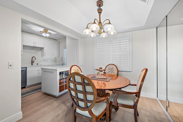 dining room with wine cooler, an inviting chandelier, sink, and light hardwood / wood-style flooring