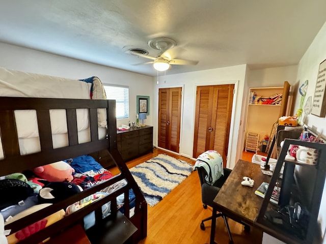 bedroom featuring two closets, wood-type flooring, and ceiling fan