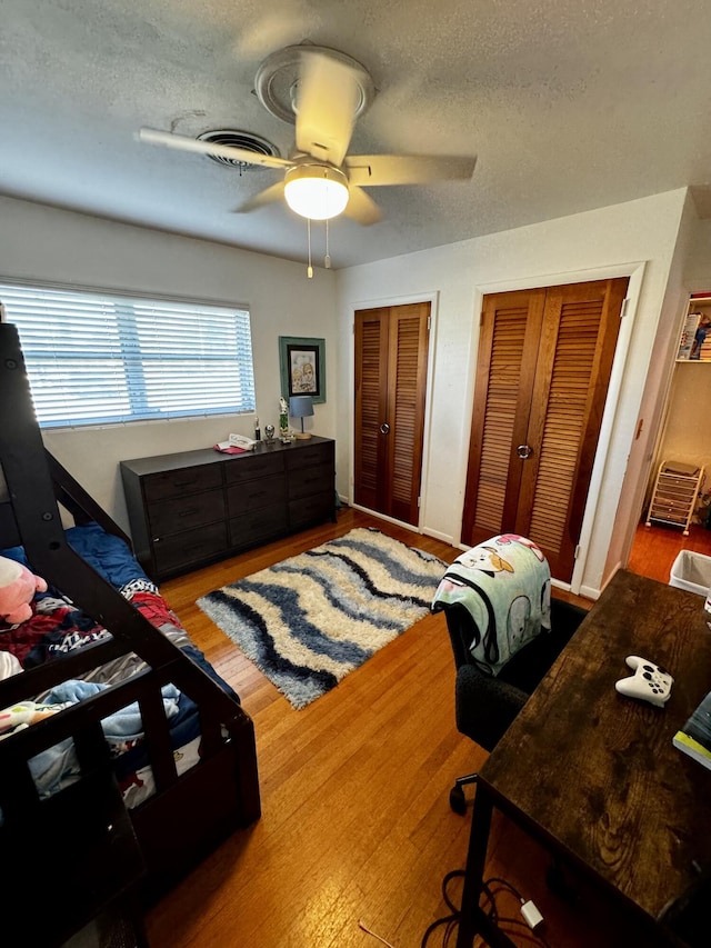 bedroom featuring ceiling fan, wood-type flooring, a textured ceiling, and two closets