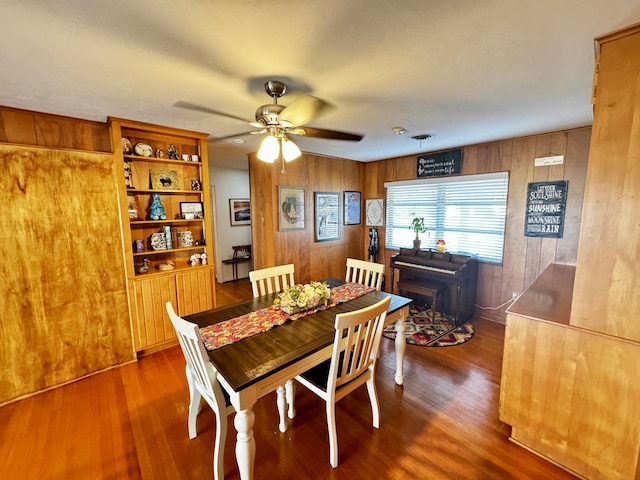 dining room featuring hardwood / wood-style flooring, ceiling fan, and wood walls