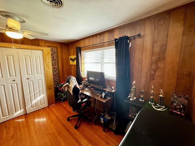 office featuring wood-type flooring, ceiling fan, and wooden walls