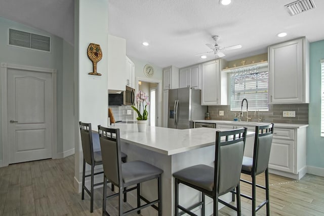 kitchen featuring a kitchen bar, sink, kitchen peninsula, stainless steel appliances, and white cabinets