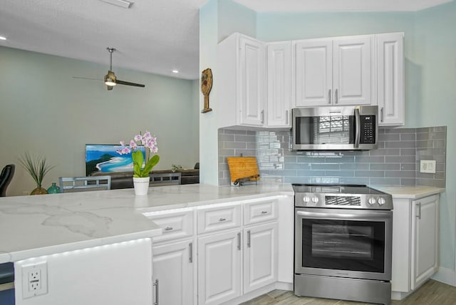 kitchen with light hardwood / wood-style flooring, appliances with stainless steel finishes, light stone counters, white cabinets, and decorative backsplash