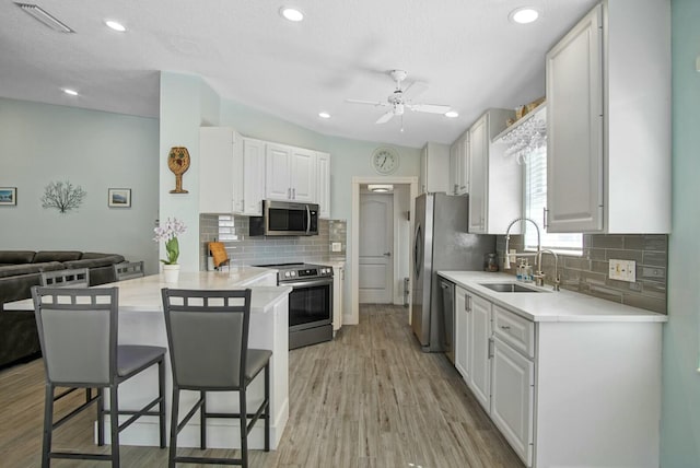 kitchen featuring appliances with stainless steel finishes, sink, white cabinets, a kitchen bar, and kitchen peninsula