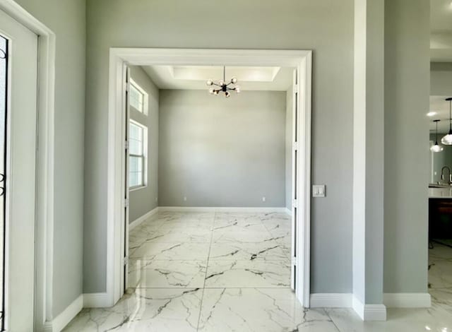 interior space featuring an inviting chandelier, marble finish floor, and baseboards