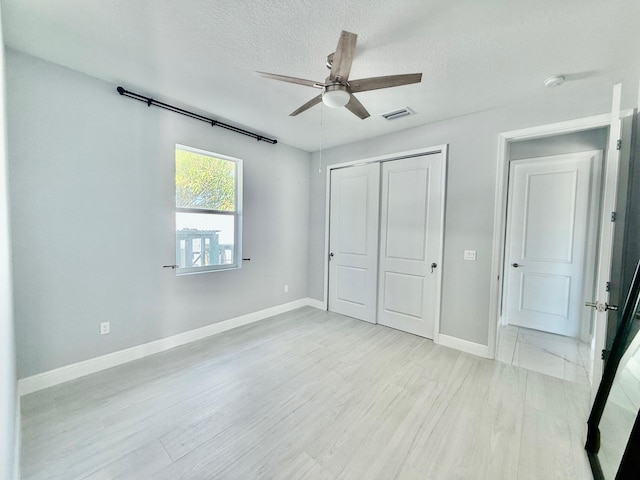 unfurnished bedroom with a textured ceiling, visible vents, baseboards, a closet, and light wood-style flooring