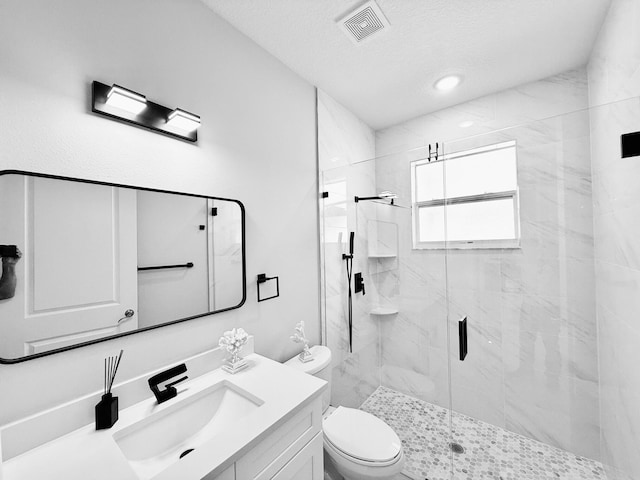 bathroom featuring a textured ceiling, toilet, vanity, visible vents, and a marble finish shower