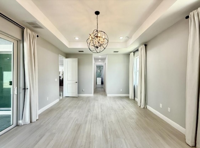interior space with light wood finished floors, a chandelier, baseboards, a tray ceiling, and visible vents